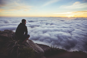 man sitting on a mountain peak above the cloud