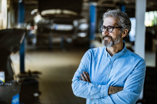 AutoFix Auto Shop Coaching Philosophy; Professional, handsome middle aged man with glasses looking satisfied at an auto repair shop