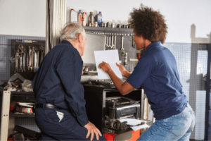 Step-By-Step Guide on How to Audit Your Repair Orders with Chris Cotton of AutoFix Auto Shop Coaching; image of African American female shop owner going over repair order with older male mechanic near shop tools and printer