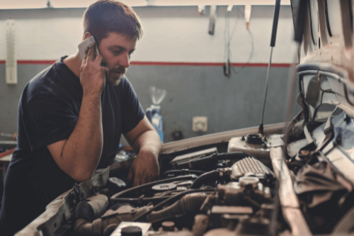 How to Boost Your Customer Service by Auditing Phone Calls with Chris Cotton of AutoFix Auto Shop Coaching; image of mechanic leaned over open hood of vehicle while on the phone
