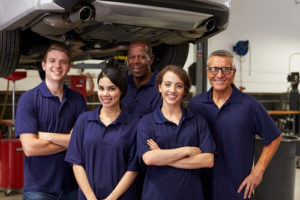 Go Beyond Cooperation with True Collaboration at Your Auto Repair Shop with Chris Cotton of AutoFix Auto Shop Coaching image of 3 male and 2 female, smiling team members of auto shop with car on lift in background