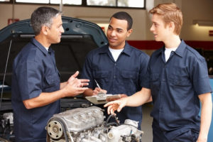Ready to Start Investing in Your Employees? Let’s Talk Career Development with Chris Cotton of AutoFix Auto Shop Coaching; image of auto shop owner explaining parts of engine outside of vehicle to two young male mechanics in shop