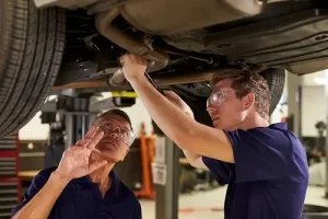 Building a Great Mentorship Program for Your Auto Repair Business | AutoFix Auto Shop Coaching. Image of a male master mechanic and a male trainee or apprentice working together underneath a car.