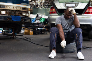 Why are Auto Technicians Leaving the Industry | AutoFix Auto Shop Coaching. Image of a tired mechanic with several cars in his background.