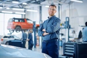 Coaching on auto technician retention strategies from AutoFix Auto Repair Shop Coaching. Image of a handsome car mechanic posing for service, he's engaged and satisfied.