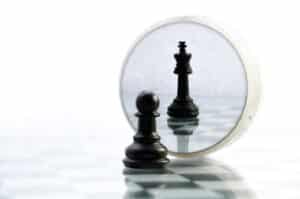 Illustration from AutoFix Auto Repair Shop Coaching. Image depicting a chessboard with a pawn strategically placed in a corner, symbolizing the concept of self-imposed corners in the auto repair business, inspired by Sun Tzu's wisdom. The pawn is reflected in a mirror as a king, representing the transformative power of strategic thinking and innovation in overcoming challenges.