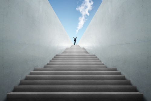 A photograph of a business climbing a ladder, reaching the top with a smile, symbolizing success and achievement in the transition from AutoFix Auto Repair Shop Coaching