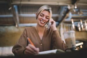 Service Writer at Auto Repair Shop: Key Role Explained. Image of a smiling service writer taking notes while on a phone call, highlighting the importance of clear communication and customer service in ensuring effective auto repair shop operations and customer satisfaction.