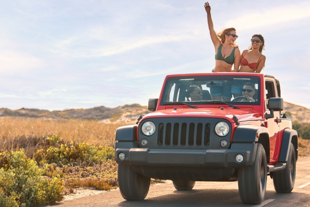 Summer Road Trip Essentials near me in North Richland Hills, TX, by AutoFix Auto Shop Coaching. Image of a red Jeep with two women enjoying a summer drive, showcasing the excitement and freedom of a well-prepared road trip recommended by AutoFix Auto Shop Coaching in North Richland Hills, TX.