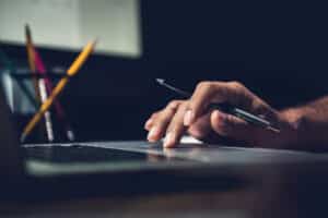 Selling service by AutoFix- Auto Shop Coaching. A hand of a man with a pen while using laptop computer