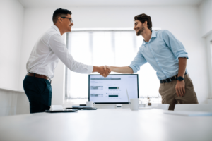 automotive business coaching, United States. Two professionals shaking hands across a conference table in a modern office setting.