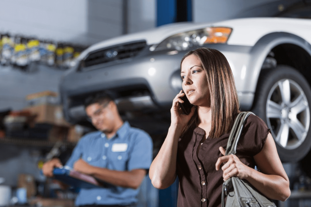 customer conflict, AutoFix Auto Shop Coaching. Woman on the phone in an auto repair shop while a mechanic takes notes in the background.