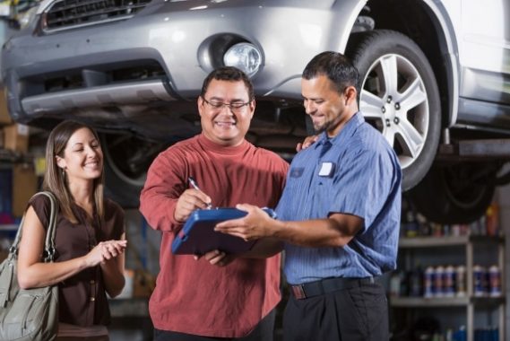 Building Trust and Shop Culture: Key Steps to Success in the Auto Repair Industry. Two men and a woman examine a clipboard in a car garage, surrounded by tools and vehicles, discussing important details.